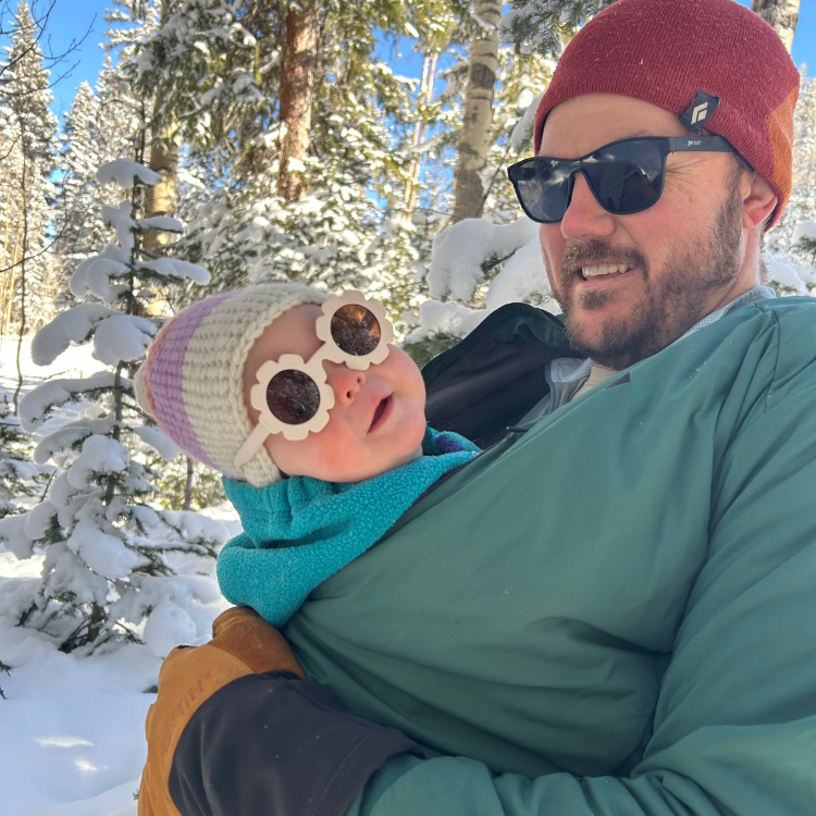 One of the owners of the Gear Junction, Cole, holding a baby in a snowy forest