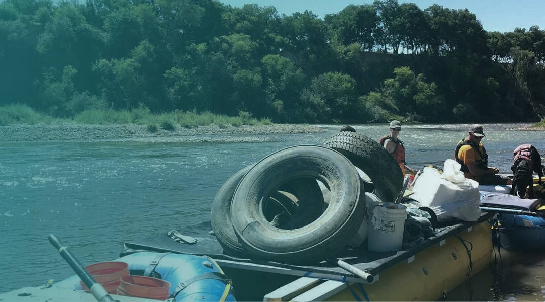 The Grand Valley River Cleanup crew remove tires and other trash out of the Colorado River via raft, surrounded by trees