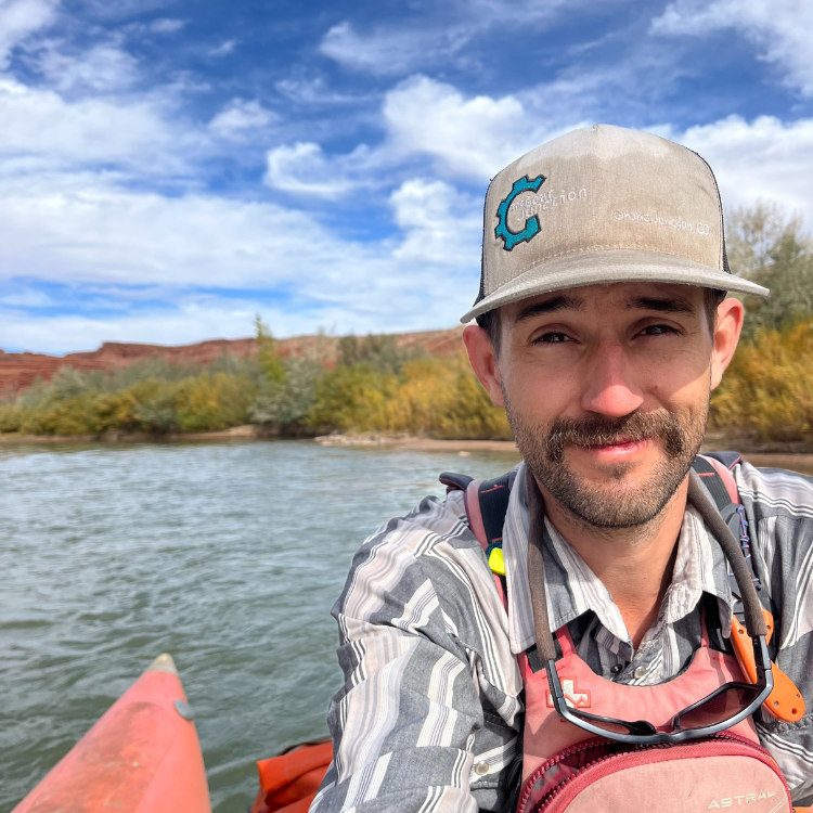 Jacob, one of Gear Junction's owners, wearing a cap and life jacket on a boat with a scenic background