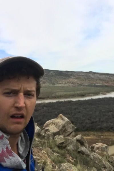 A man with a surprised look in the foreground, with a river landscape in the background