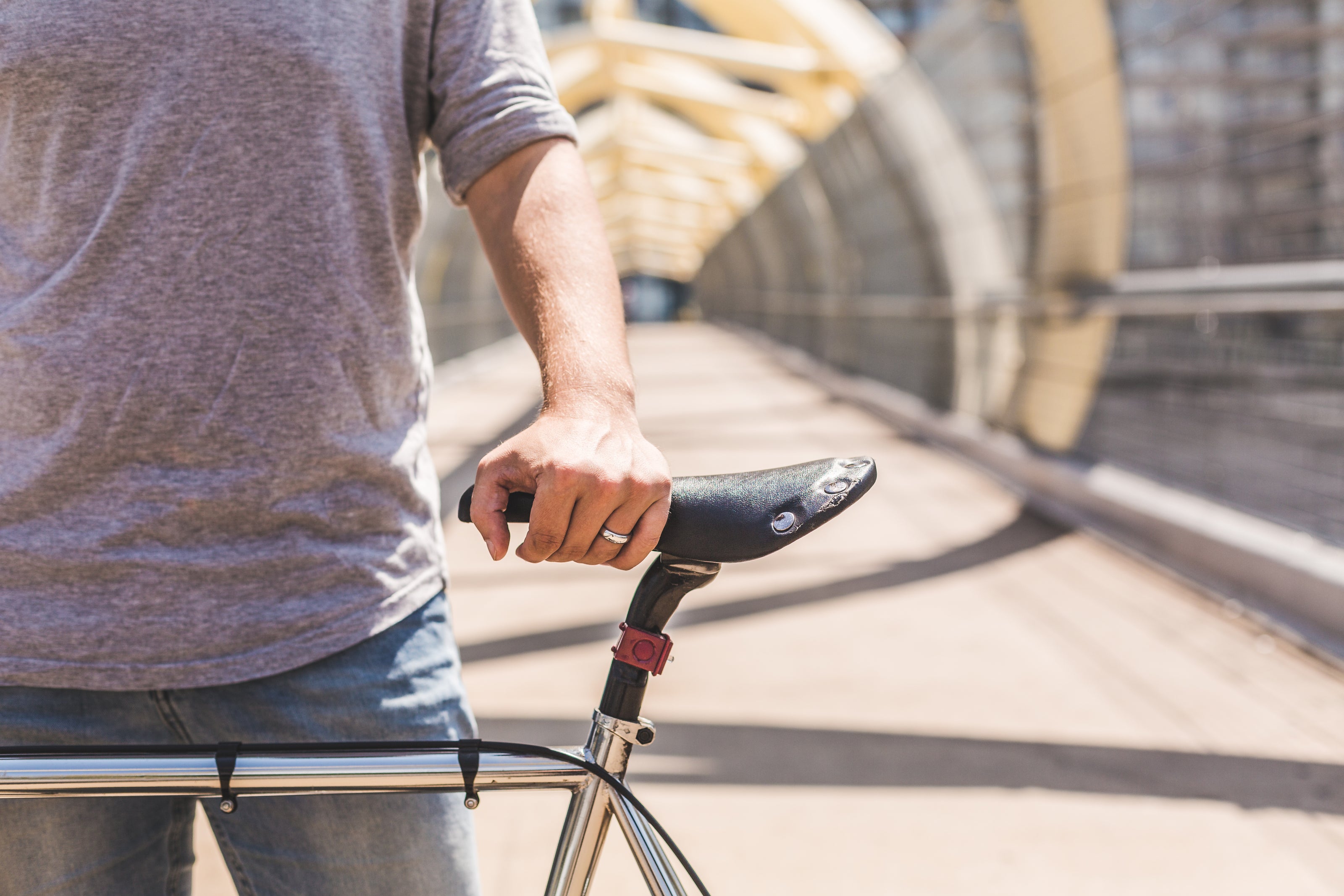 A man's hand holds a bike upright with a pedestrian walkway in the background.