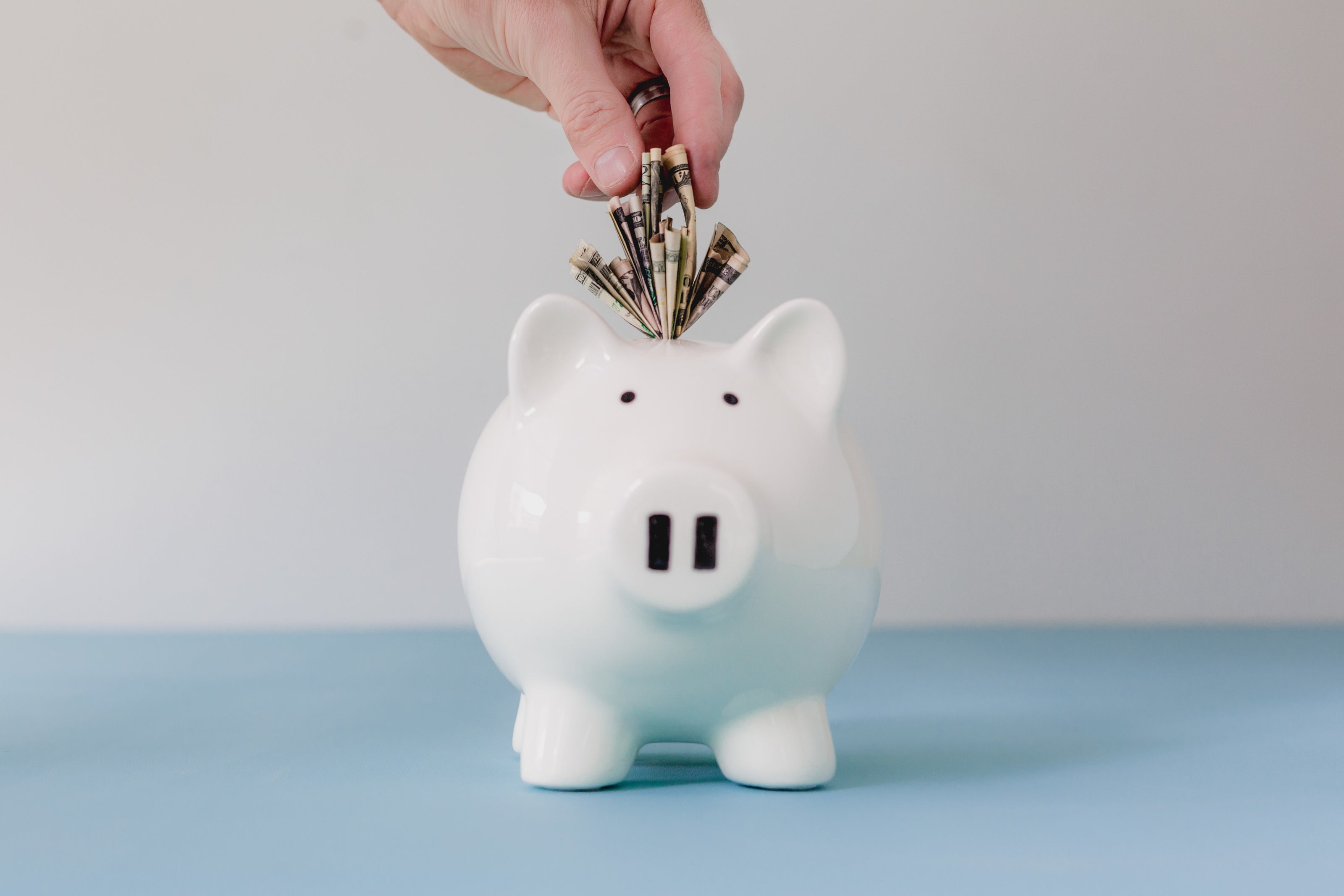 A hand putting money into a white piggy bank on a gray background